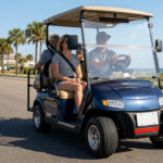 A street legal golf cart with a license plate, LED headlights, and side mirrors driving on a coastal public road alongside traffic.