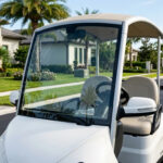 A street-legal low-speed vehicle with a DOT-approved safety glass windshield and integrated side mirrors, parked in a residential gated community.