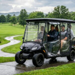 A black 4-passenger golf cart equipped with a high-clarity waterproof enclosure driving through a rainy golf course, showcasing weather protection and passenger comfort.