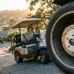 A high-performance golf cart disc brake conversion showing a slotted rotor and caliper, with a golf cart navigating a steep residential hill in the background for safety.